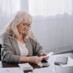 senior woman sitting at table with paperwork and counting money