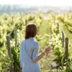 femme qui boit du vin devant des vignes